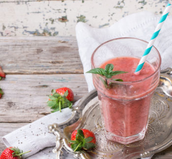 Glass of red strawberry smoothie with chia seeds, served with retro cocktail tube, fresh mint and strawberries over wooden table